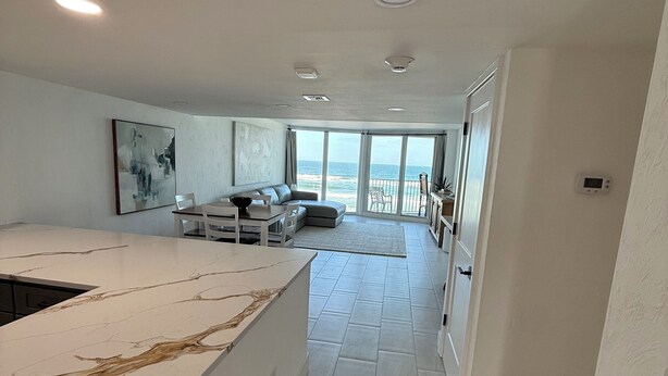 A modern kitchen with a marble countertop, a dining area with a sofa, and a view of the ocean through large windows. - Charming beachfront condo, Daytona Beach Shores (Daytona Beach Shores)