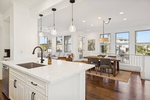 Une cuisine spacieuse dotée d’un grand îlot central, de luminaires suspendus modernes et offrant une vue sur l’extérieur grâce à de grandes fenêtres.