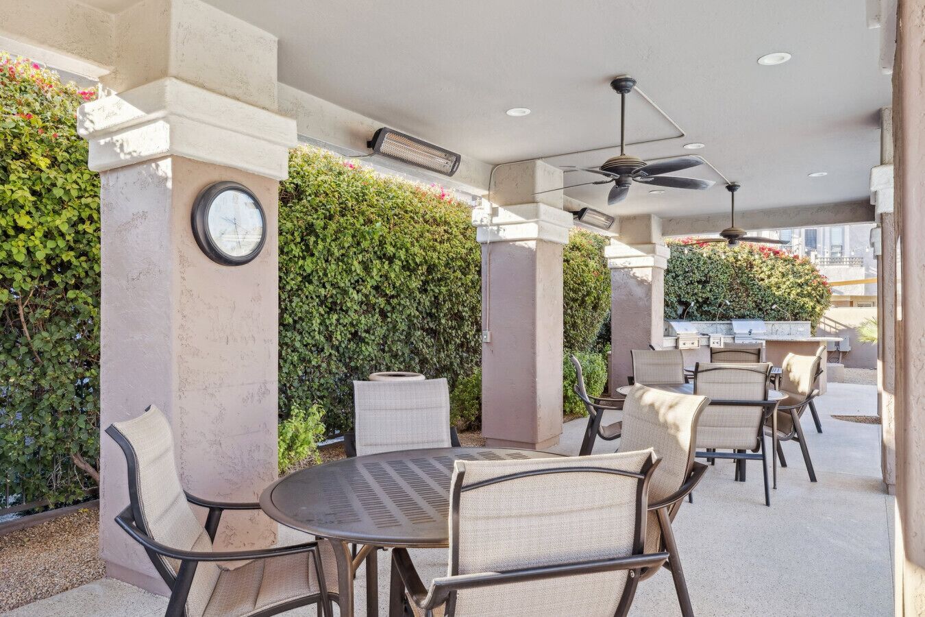An outdoor patio with round tables and chairs, a ceiling fan, and a wall of greenery.