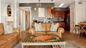 Un salon avec un canapé en cuir marron, un tapis à motifs et un coin repas comprenant une table et des chaises en bois.