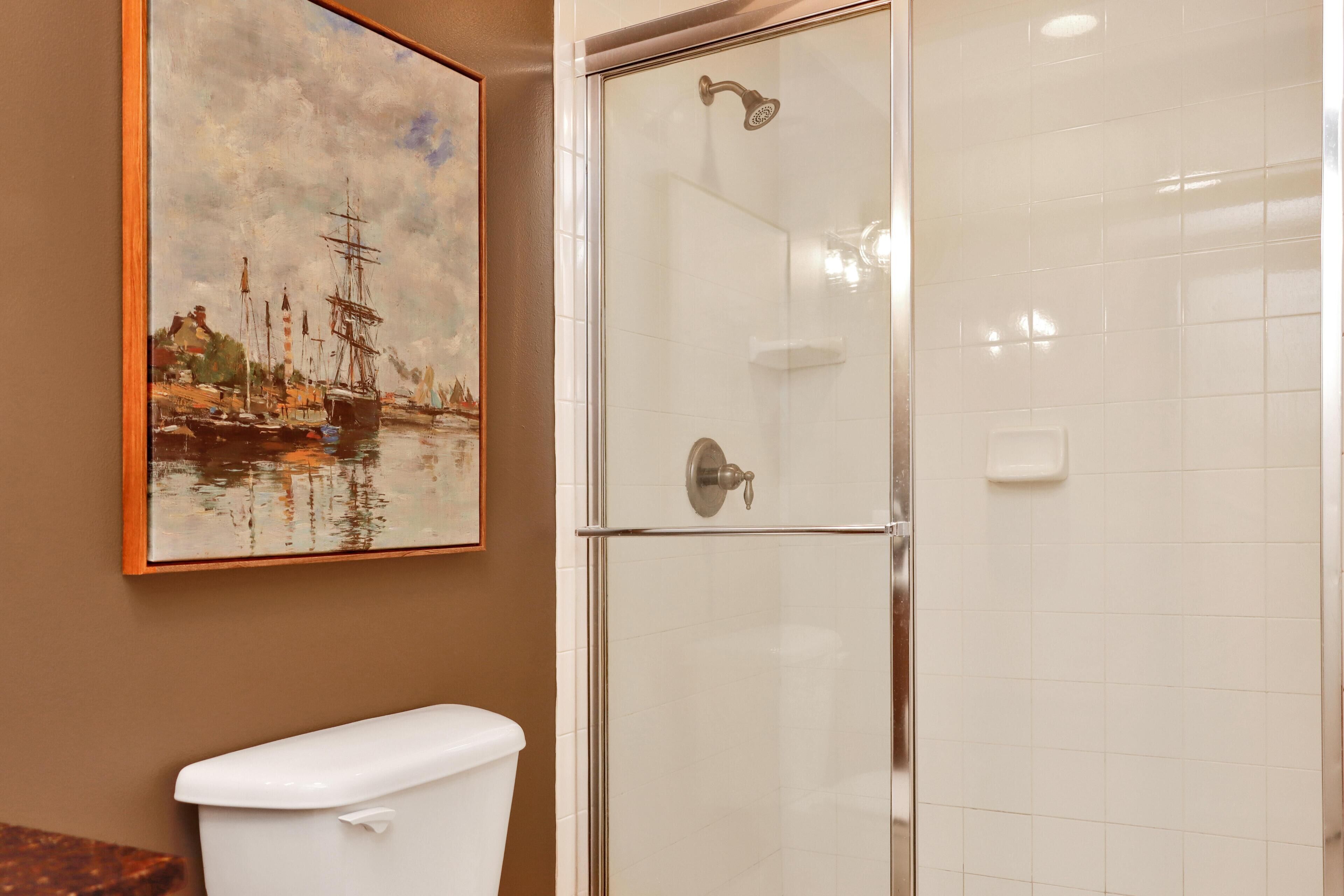 Une salle de bain avec une douche à parois de verre, des toilettes et un tableau représentant un paysage portuaire accroché au mur.