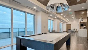 Mesa de bilhar numa sala moderna com janelas amplas e vista para o mar.