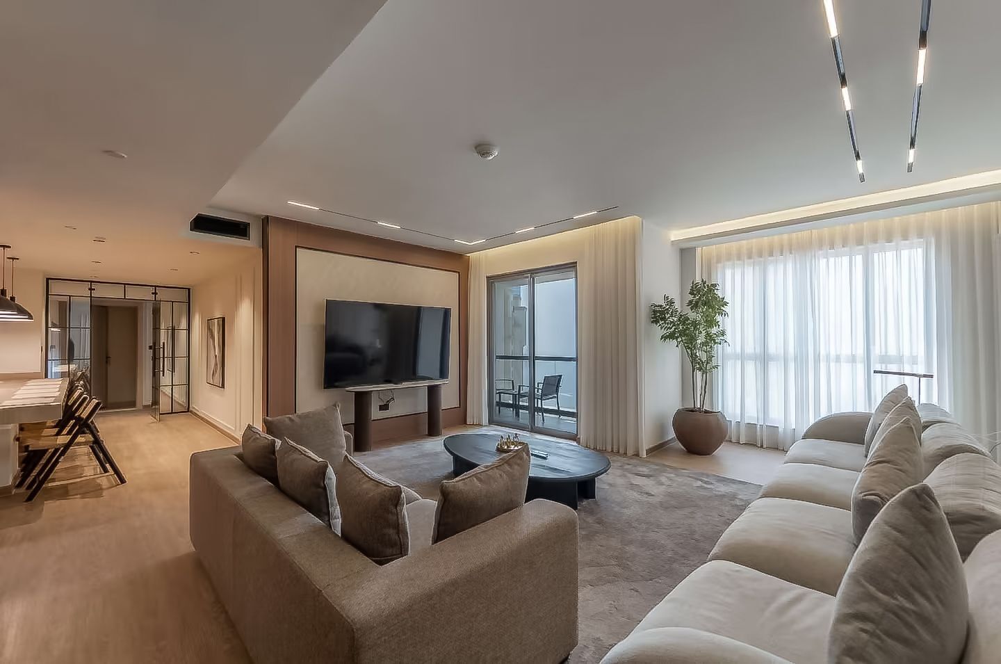 Una sala de estar moderna con sofá, mesa de centro, televisor y un amplio ventanal con cortinas.