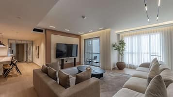 Een moderne woonkamer met een bank, salontafel, televisie en een groot raam met gordijnen.