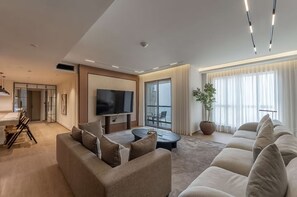 Ein modernes Wohnzimmer mit einer Couch, einem Couchtisch, einem Fernseher und einem großen Fenster mit Vorhängen.