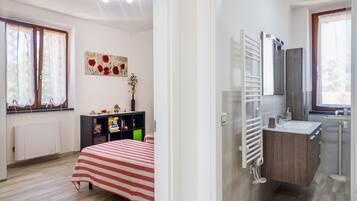 Een slaapkamer met een bed, een kast, een radiator en een raam met gordijnen.