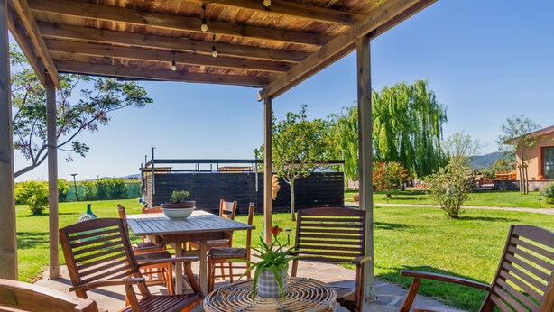 An outdoor patio with a wooden table and chairs, surrounded by greenery and a clear sky. - Podere 660 – Il Giuggiolo Apartment (Grosseto)