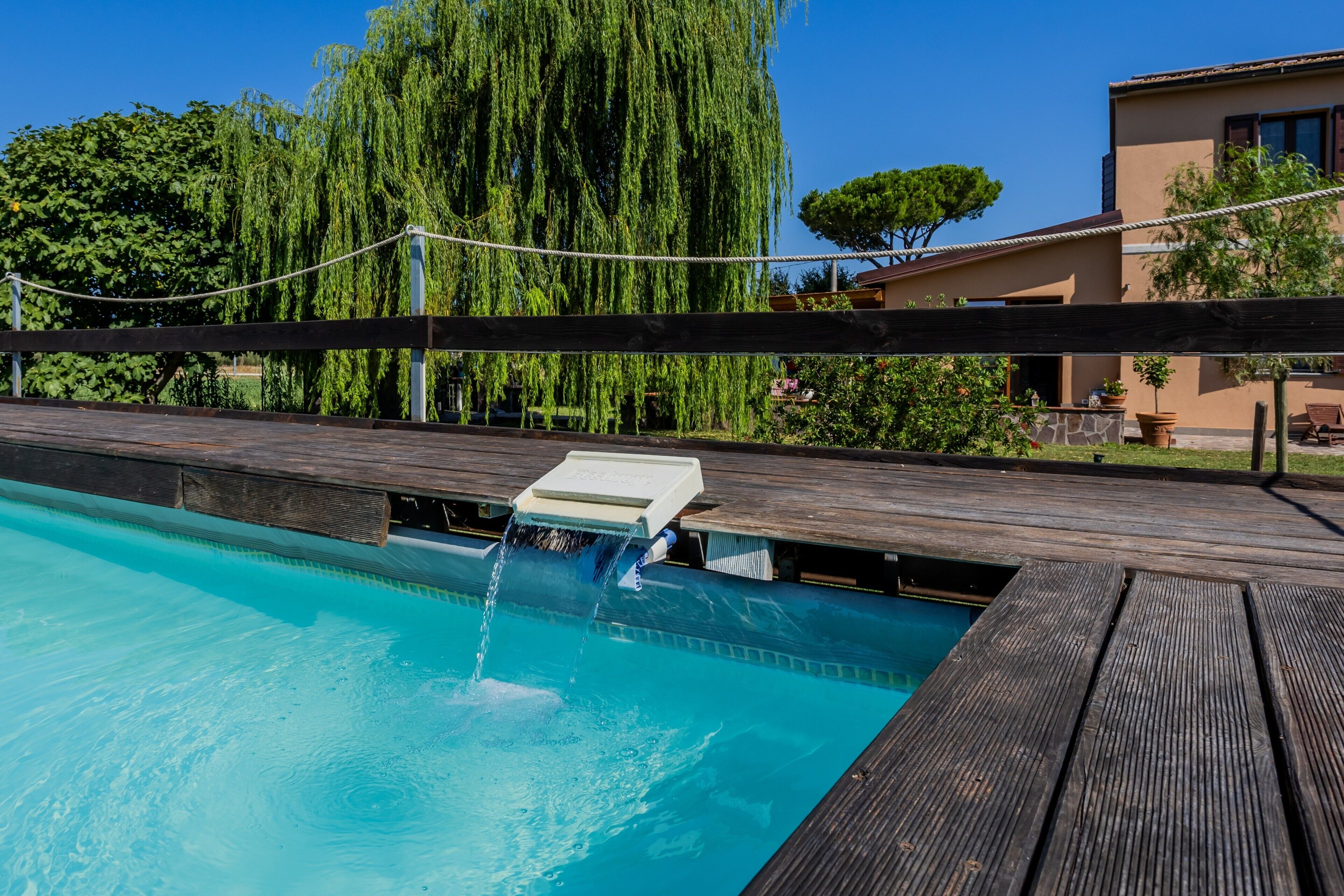 A swimming pool with a wooden deck and a water feature.