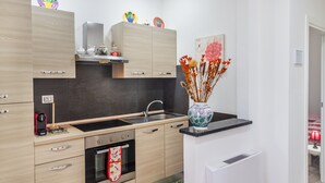 A modern kitchen with wooden cabinets, a black countertop, a sink, an oven, and a vase with dried flowers. - Podere 660 – Il Giuggiolo Apartment (Grosseto)