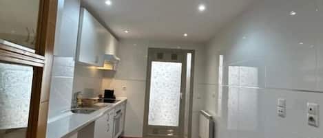 A narrow kitchen with white cabinets, a wooden countertop, and a black mat on the floor.
