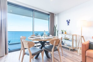 A modern dining area with a large window overlooking the sea, a round table with chairs, and a glass cabinet with decorative items. - Xavelha Clifftop by Atlantic Holiday (Câmara de Lobos)