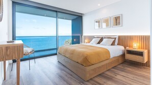 Un dormitorio moderno con una cama grande, una mesita de noche de madera, una silla y vista al océano.