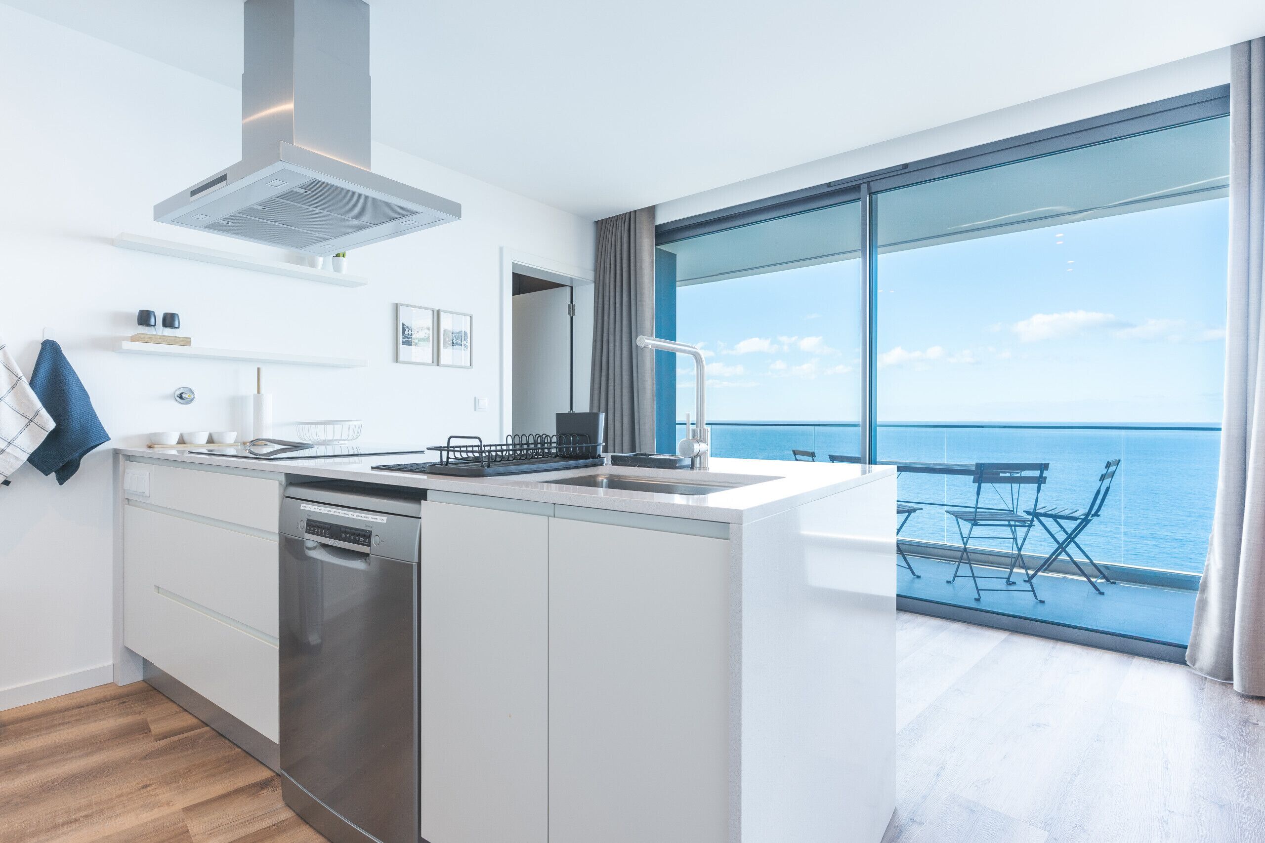 A modern kitchen with a dishwasher, a stove, and a sink. There is a large window with a view of the ocean.