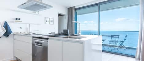 A modern kitchen with a dishwasher, a stove, and a sink. There is a large window with a view of the ocean.
