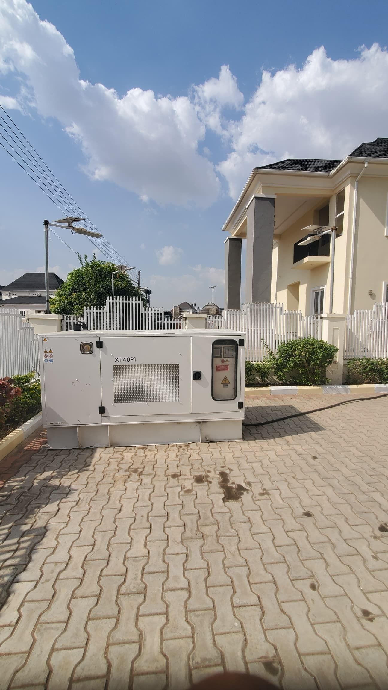 A utility box labeled XP40P1 on a paved area with a white fence and residential buildings in the background.