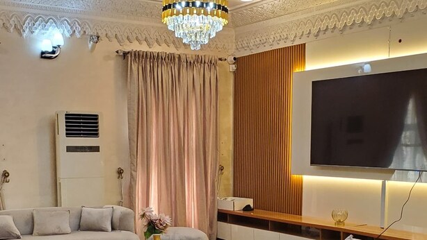 Un salon moderne avec un lustre, un ensemble de canapés, une table basse et un téléviseur à écran plat.