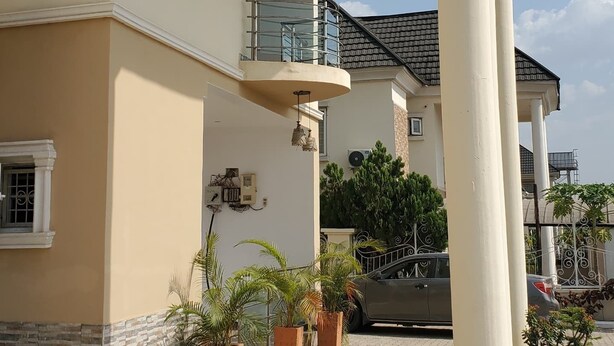 A multi-story building with a covered entrance, potted plants, and a car parked outside. - Sunabi Hotels and Apartments  (Abuja)