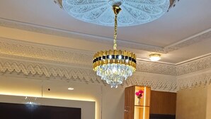 A modern living room with a large flat-screen TV, a chandelier, and a sofa. - Sunabi Hotels and Apartments  (Abuja)