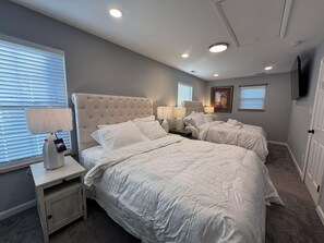 Een slaapkamer met twee bedden, een televisie en een raam met zonwering.