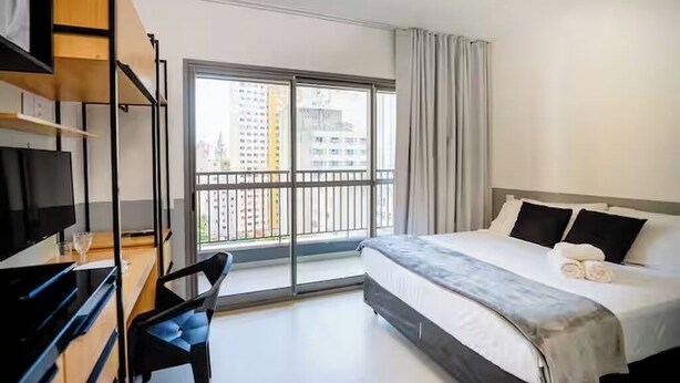 Ein modernes Hotelzimmer mit einem großen Bett, einem Schreibtisch mit Stuhl, einem Fernseher und einem Balkon mit Stadtblick.