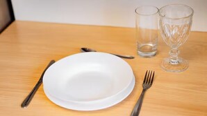 Ein weißer Teller, eine Gabel, ein Löffel und zwei Gläser auf einem Holztisch.