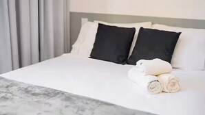 Ein ordentlich bezogenes Bett mit weißen und schwarzen Kissen, ein aufgerolltes weißes Handtuch und eine Bettdecke mit Marmor-Muster.
