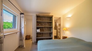 Una camera da letto con un letto, una finestra, un mobiletto a mensole di legno e una lampada fissata al muro.