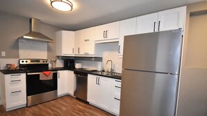 A modern kitchen with white cabinets, stainless steel appliances, and a wooden floor. - Benbow Suite (Hinton)