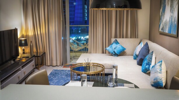 A modern hotel room with a sofa, a dining table, a TV, and a large window with curtains. - Modern 1BR Downtown - Dubai Mall Walk (Dubai)