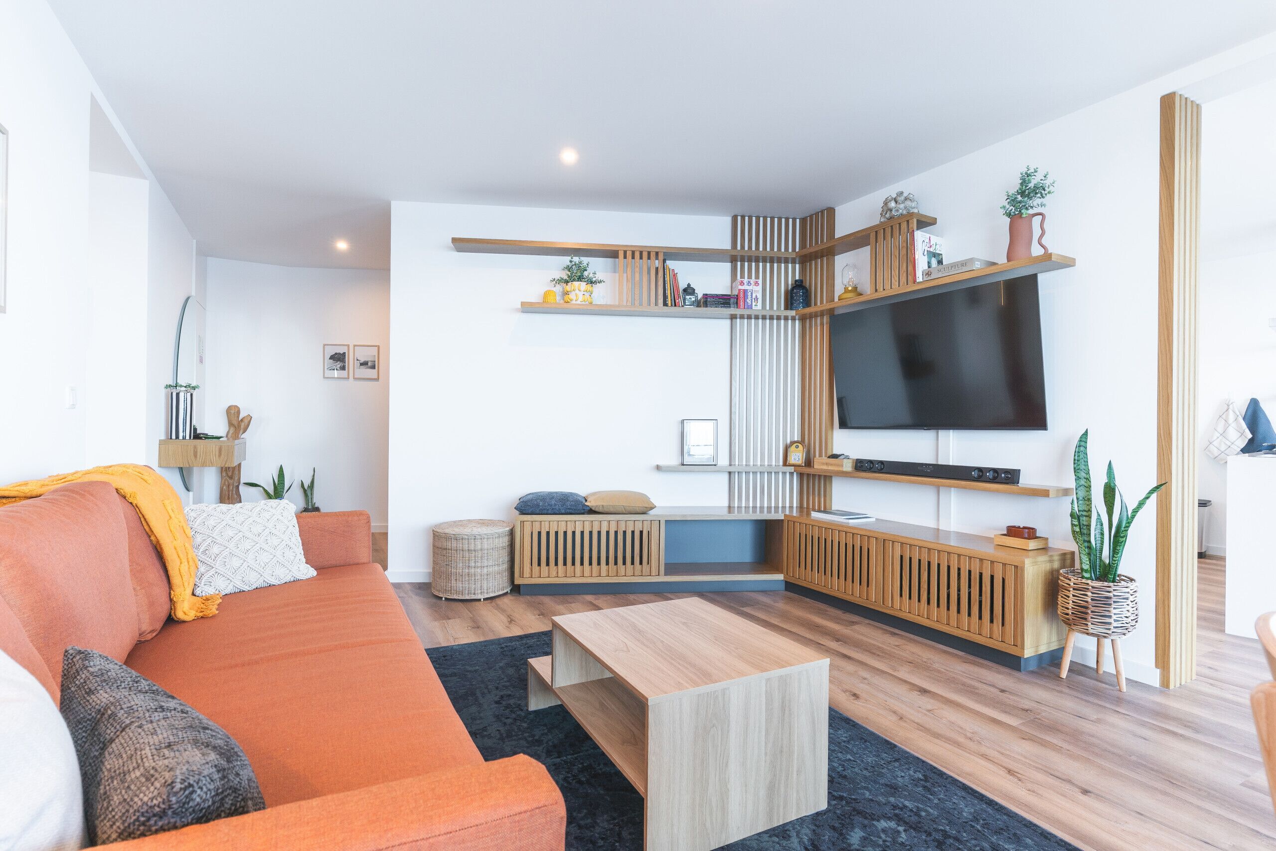 Una sala de estar moderna con sofá, mesa de centro y televisor. Se observan estantes con plantas y libros.