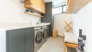 A compact kitchen with a washing machine, a small trash bin, and a vacuum cleaner. - Xavelha Clifftop by Atlantic Holiday (Camara de Lobos)