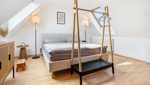 Un dormitorio con techo inclinado, una cama con estructura de madera, una lámpara de pie, una mesita pequeña y un cuadro en la pared.