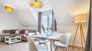 Una sala moderna con una mesa de comedor, sillas blancas, un sofá y una lámpara de pie.