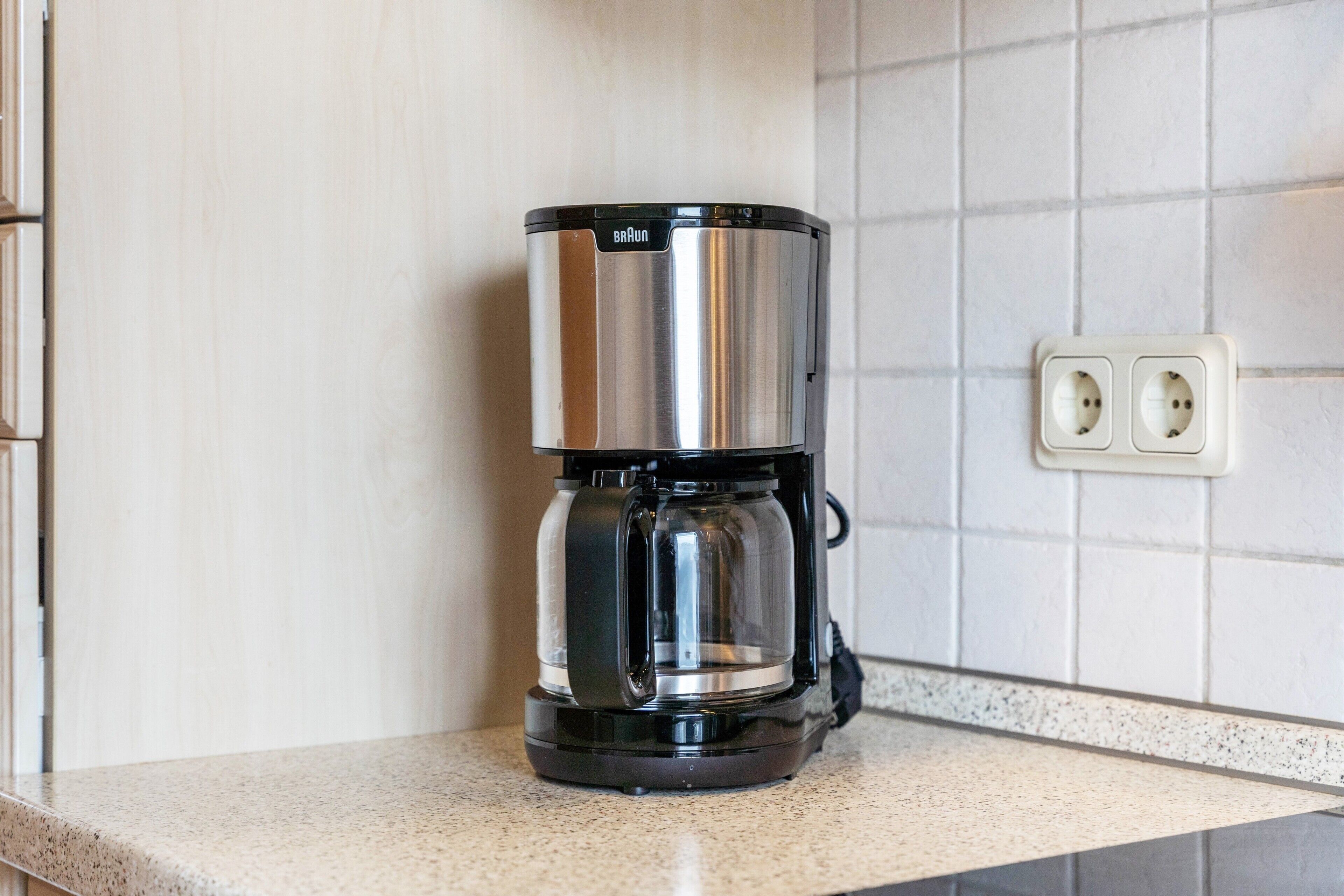 A kitchen with a coffee maker on the counter, a tiled backsplash, and a double electrical outlet.