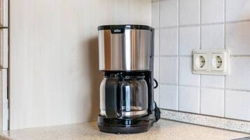 A kitchen with a coffee maker on the counter, a tiled backsplash, and a double electrical outlet.