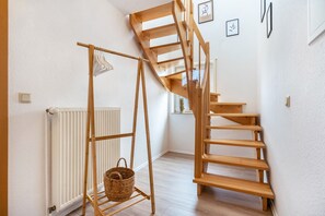 Eine hölzerne Wendeltreppe in einem Raum mit weißen Wänden, einem Heizkörper und einem Korb auf einem Holzgestell.