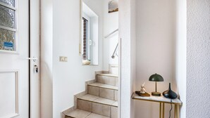 Una escalera con baldosas color beige, una puerta blanca y una pequeña mesa con una lámpara y adornos.