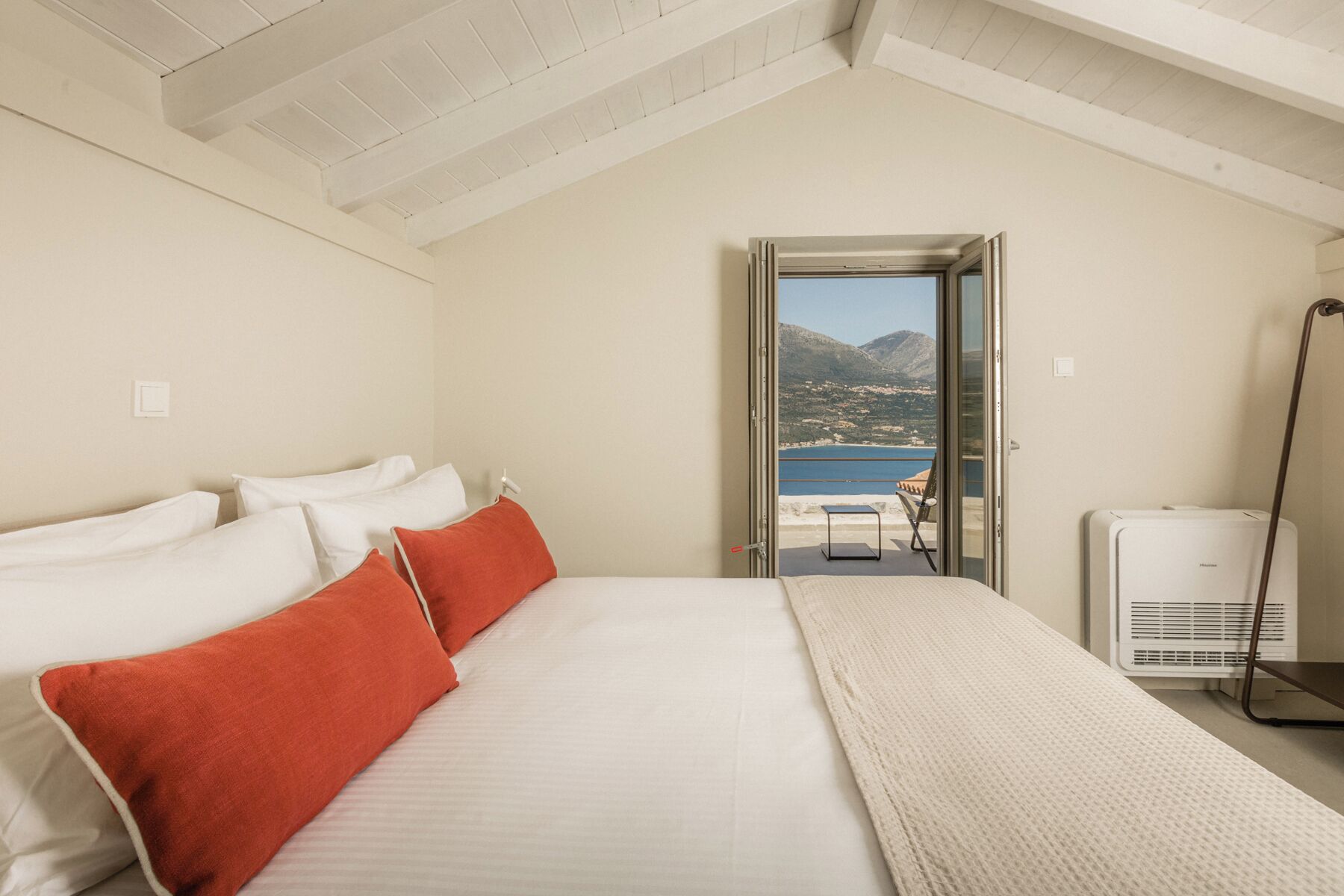 Ein Schlafzimmer mit Bett, Kissen, Heizung und Blick auf ein Gewässer und Berge.