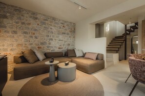A modern living room with a stone wall, a sectional sofa, a round coffee table, and a staircase. - Nest Limeni (East Mani)