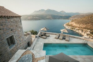 A stone building with a pool and lounge chairs overlooking a body of water and mountains. - Nest Limeni (East Mani)