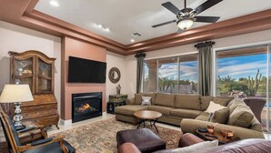 Ein Wohnzimmer mit Kamin, Sofa, Sessel und Deckenventilator.