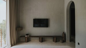 Una stanza dal design minimalista con un'ampia finestra, una TV a schermo piatto fissata alla parete, una panca in legno e un tavolino con una lampada.
