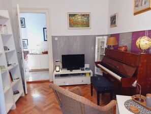 Un soggiorno con televisione, pianoforte, poltrone in vimini e un mappamondo su un tavolo.