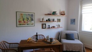 Una stanza accogliente con un tavolo da pranzo in legno, sedie in vimini, una libreria con diversi oggetti, un quadro incorniciato e una finestra con persiane.