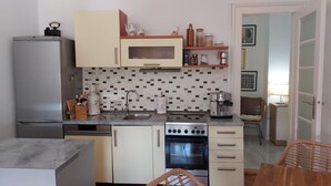 Una cucina compatta con frigorifero, microonde, fornello e forno. Sono presenti armadietti, un lavandino e diversi utensili da cucina.