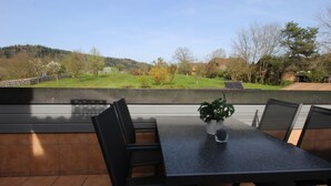 An outdoor patio with a table and chairs, a potted plant, and a view of a green landscape with trees and a hill. - Cozy 2-room apartment in the southern Black Forest (Steinen)