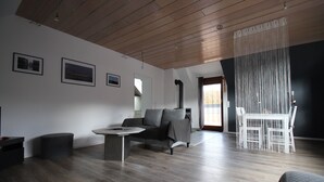 A modern living room with a wooden ceiling, a grey sofa, a round coffee table, and a white dining table with chairs. - Cozy 2-room apartment in the southern Black Forest (Steinen)