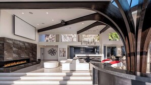 Een modern interieur met een open haard, witte banken, een keukenhoek en een groot raam.