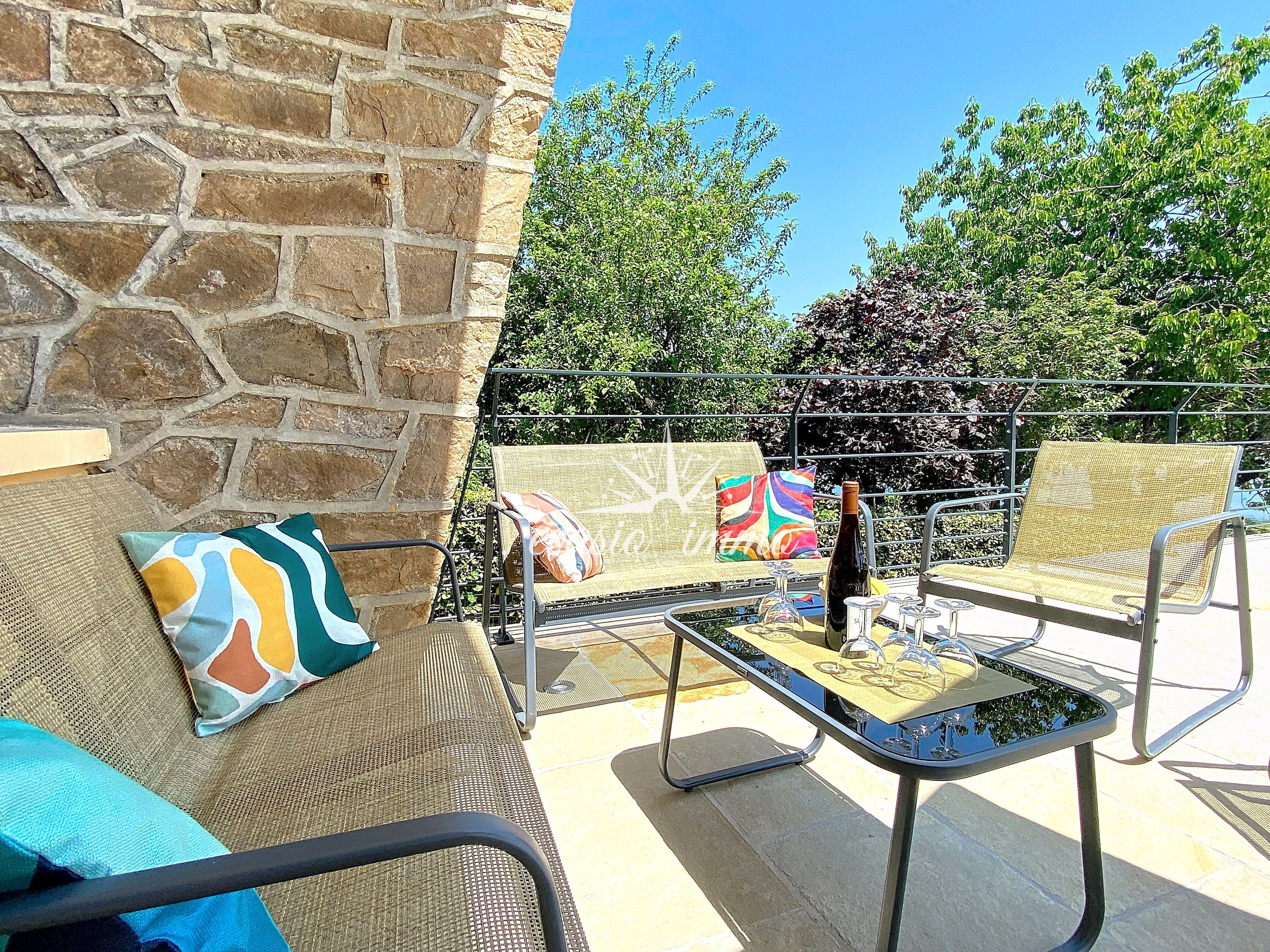 An outdoor seating area with wicker furniture, a stone wall, and a view of trees.