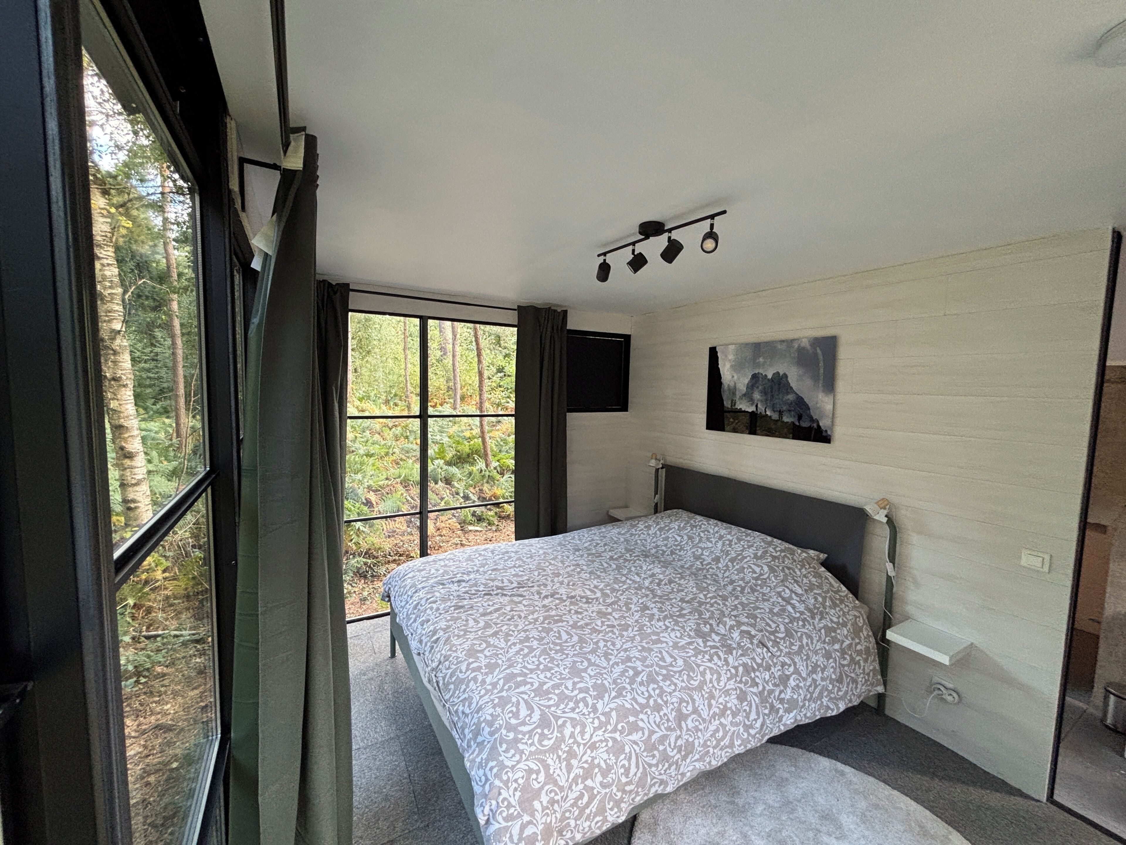 Une chambre à coucher avec un grand lit, une fenêtre avec des rideaux, un tableau accroché au mur et un luminaire au plafond.